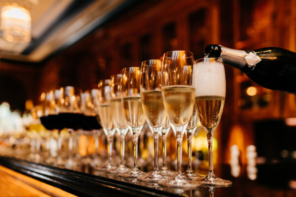 Row of glasses filled with champagne and other beverages, someone holds bottle and fills in glasses. Bar counter. Banquet
